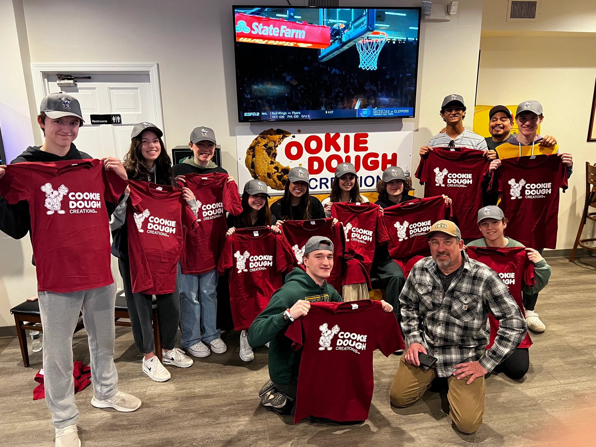 The Cookie Dough Creations team holding up shop t-shirts in front of the store sign