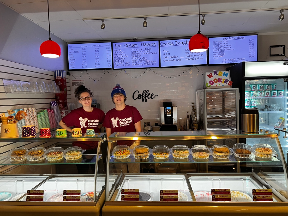 Two team members behind the dessert counter beneath the ice cream and cookie dough menu boards