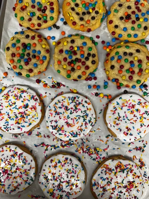 A fresh tray of M&M cookies and white-frosted sprinkle cookies cooling on parchment