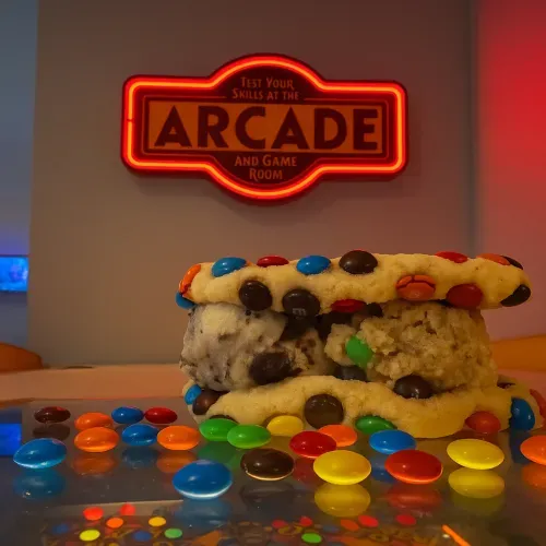 An M&M cookie dough sandwich under the neon Arcade and Game Room sign