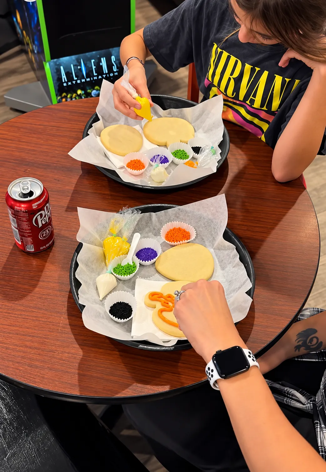 Guests decorating oversized sugar cookies with piping bags and sprinkles at a table in the game room
