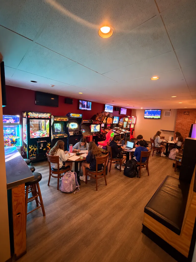 Students studying at tables in the Cookie Dough Creations game room, with arcade games along the wall