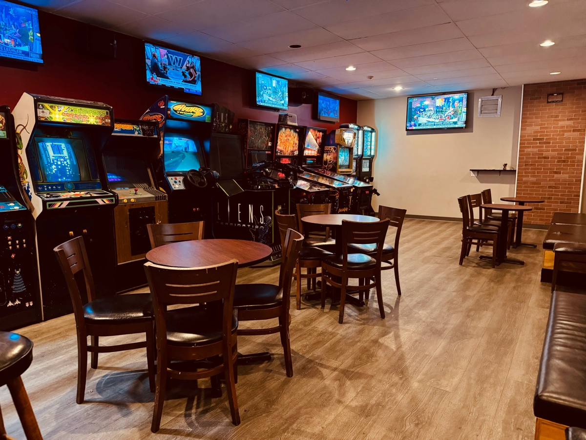 Tables and chairs beside a row of vintage arcade cabinets in the Cookie Dough Creations game room
